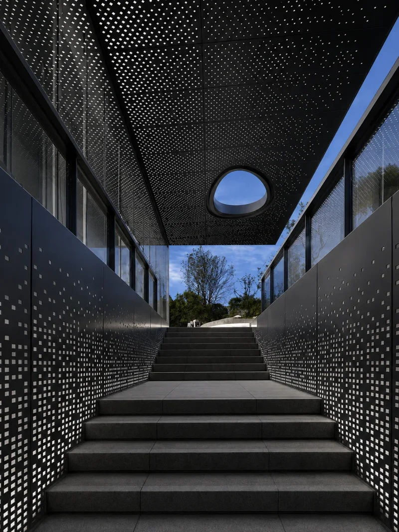 Black perforated metal ceiling panels and wall screens above a stairway