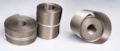 Three stainless steel reverse Dutch weave wire mesh rolls with an unrolled strip on a light background