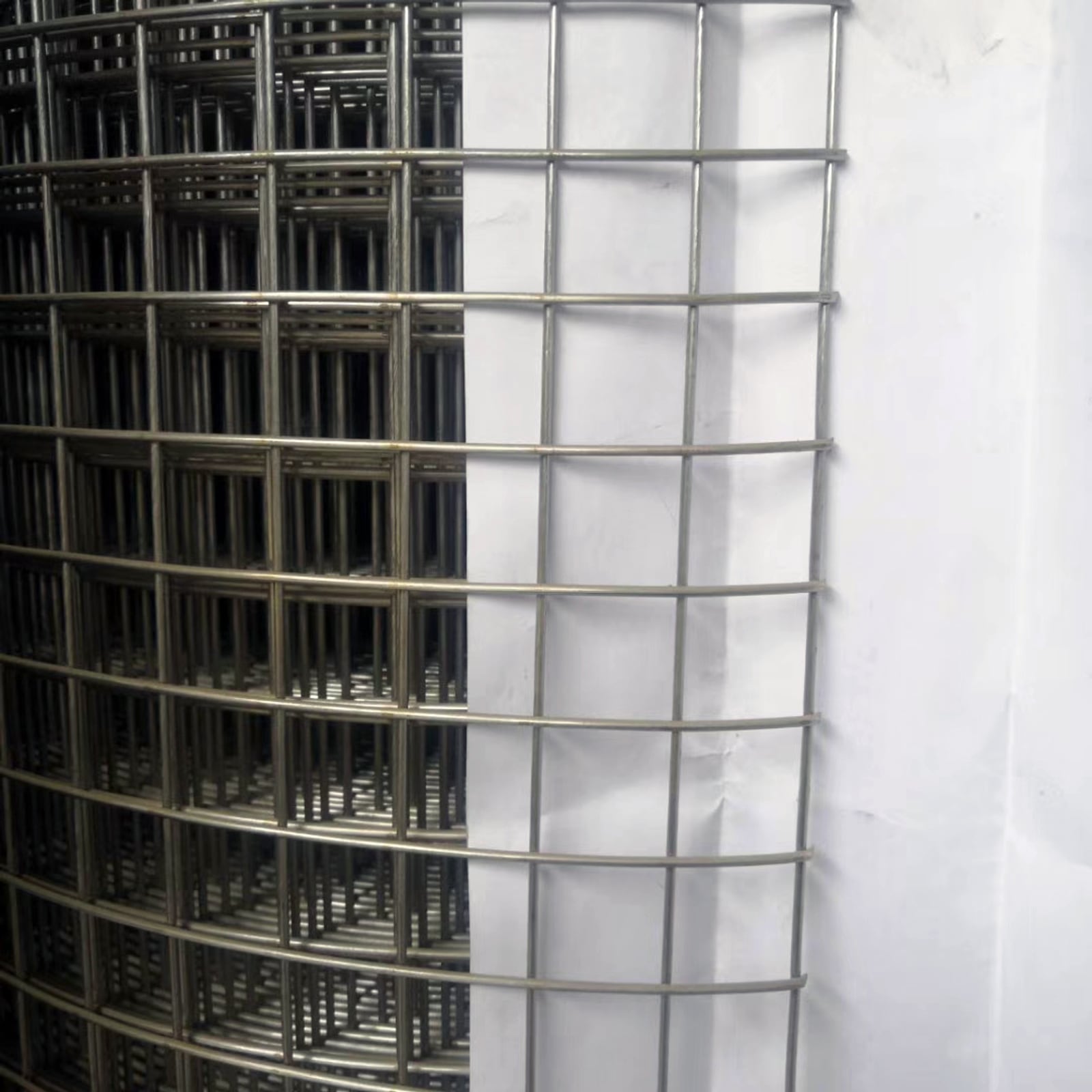 Stainless steel welded wire mesh panel with large square openings and stacked panels in the background