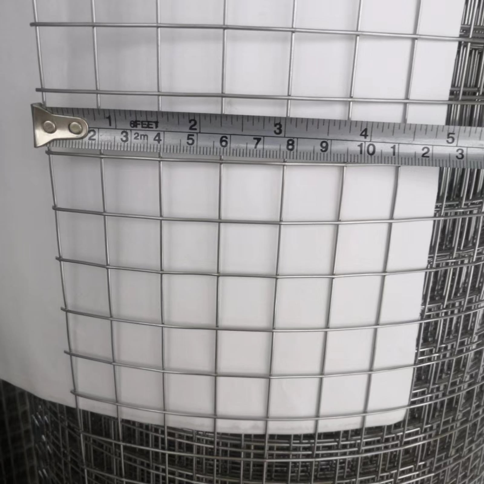 Stainless steel welded wire mesh panel with a tape measure showing the mesh opening size