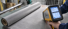 Handheld XRF analyzer testing a 304 stainless steel wire mesh roll in the factory